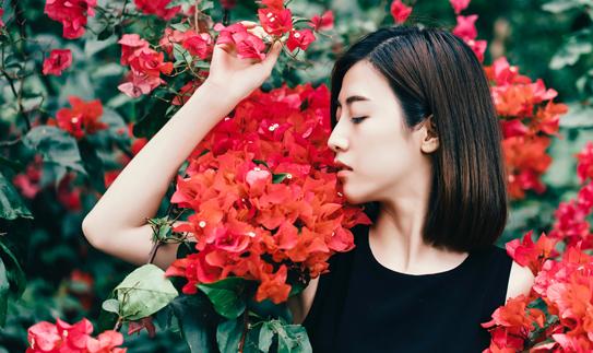 woman smelling red flowers with a relaxed expression